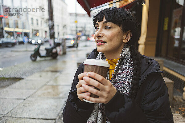 Lächelnde schöne Frau hält Einwegkaffeetasse auf der Straße