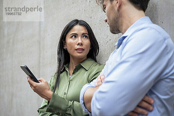 Frau mit Smartphone spricht mit Freundin vor der Wand