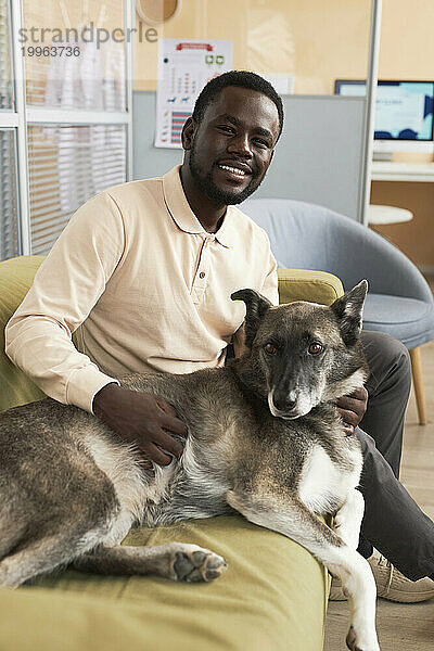 Happy young man sitting with dog on sofa in clinic