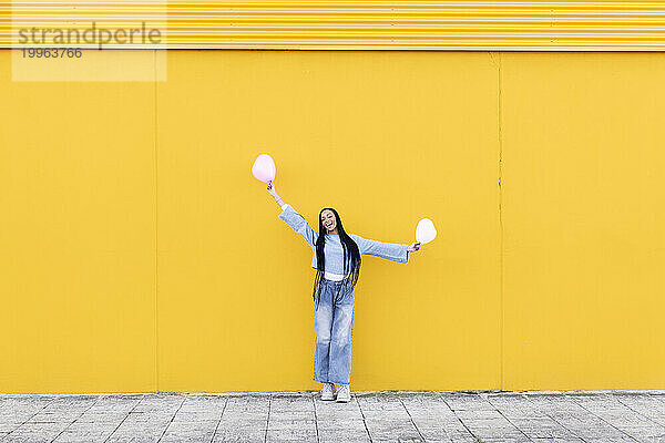 Glückliche junge Frau hält Luftballons vor gelber Wand