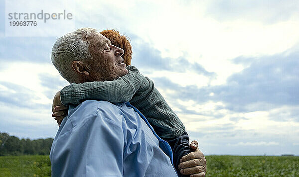 Junge umarmt Großvater unter bewölktem Himmel bei Sonnenuntergang