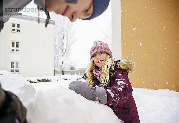 Mädchen spielt im Schnee mit Vater in der Nähe der gelben Wand