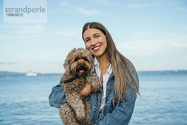 Lächelnde junge Frau mit Pudelhund am Strand