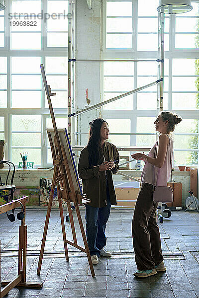 Woman and painter standing by easel in workshop
