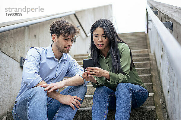 Frau teilt Smartphone mit Freund  der auf Stufen sitzt