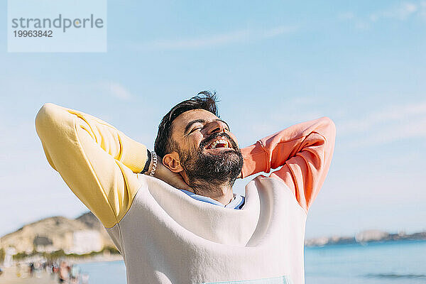 Happy man with hands behind head at beach