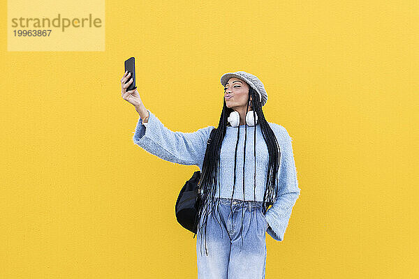 Junge Frau macht Selfie mit Smartphone vor gelber Wand