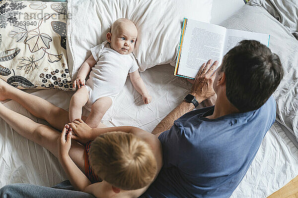 Father reading book with children on bed at home