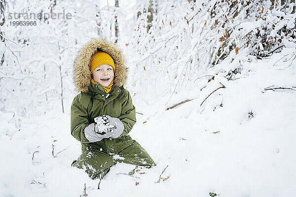 Fröhlicher Junge macht Schneeball im Winterwald