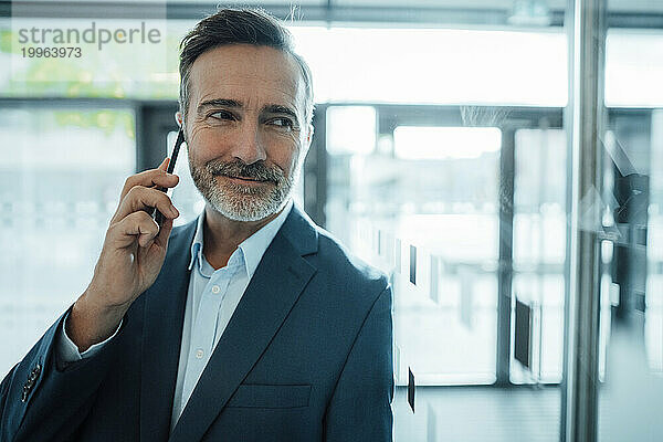 Lächelnder Geschäftsmann  der im Büro auf dem Smartphone spricht