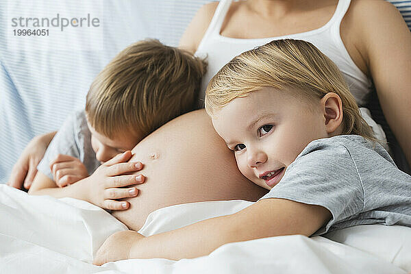 Glückliche Kinder  die sich zu Hause auf den Bauch der schwangeren Mutter stützen