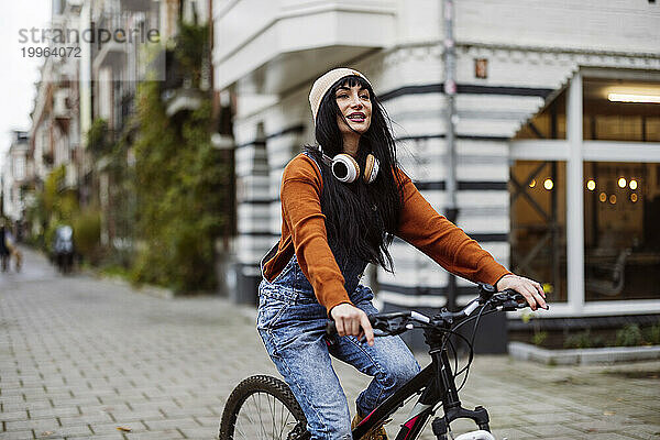Lächelnde schöne Frau  die auf einem Fußweg in der Nähe von Gebäuden Fahrrad fährt