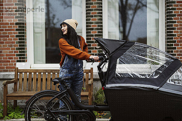 Glückliche Frau steht mit Lastenfahrrad vor dem Gebäude