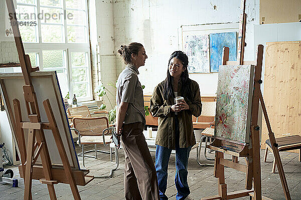 Lächelnde Frauen diskutieren über Malerei auf Staffelei im Kunstatelier