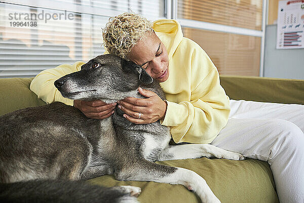 Frau umarmt Hund auf Sofa in Klinik