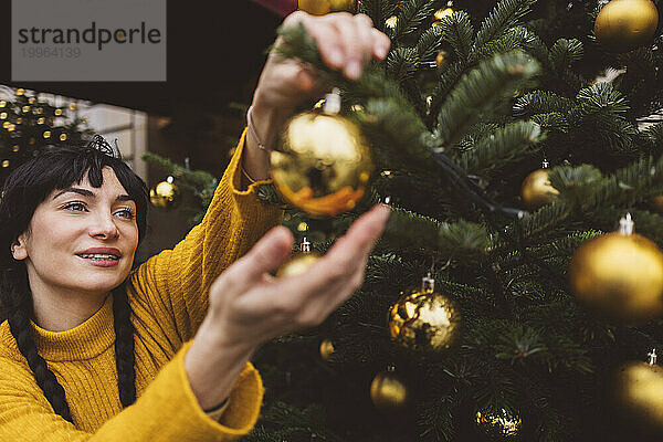Glückliche Frau schmückt den Weihnachtsbaum mit Ornamenten