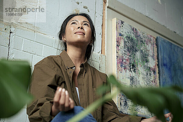 Smiling painter sitting cross-legged by paintings at art studio