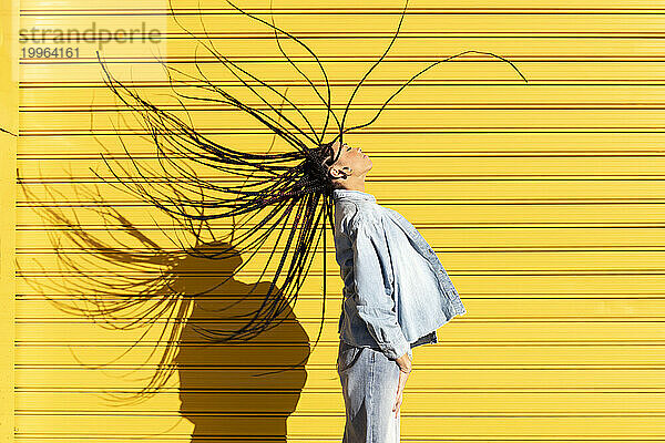 Junge Frau wirft an einem sonnigen Tag Haare vor einen Wellpappenfensterladen