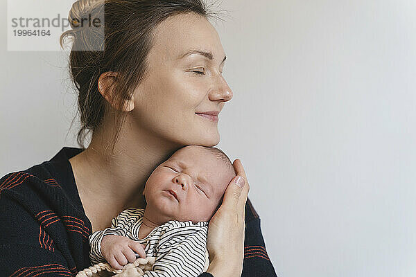 Smiling mother embracing baby boy in front of white wall