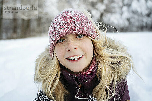 Lächelndes blondes Mädchen mit Strickmütze im Winter