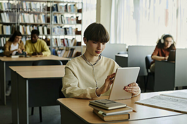 Junge Studentin nutzt Tablet-PC am Schreibtisch in der Bibliothek