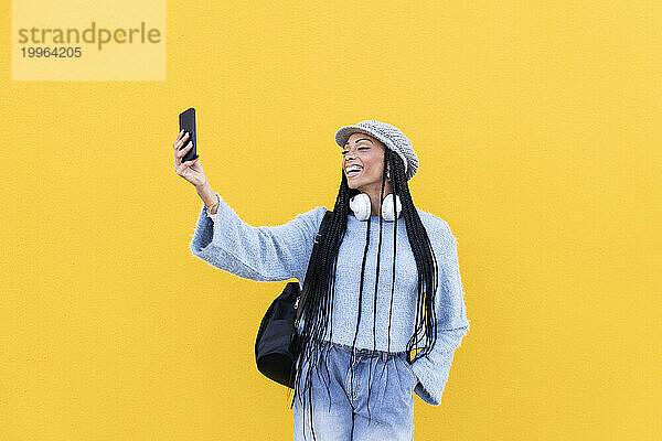 Fröhliche Frau macht Selfie vor gelber Wand