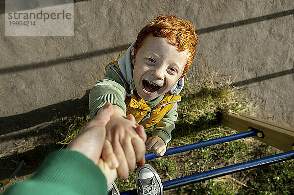 Cheerful redhead boy holding mother's hand on sunny day
