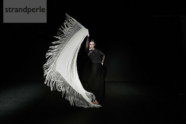 Graceful woman performing flamenco dance with shawl against black background