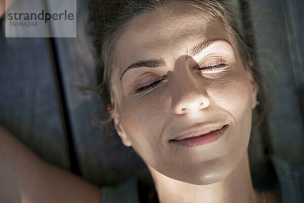 Smiling woman with eyes closed lying on bench