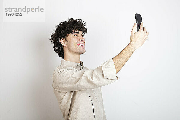 Lächelnder Mann macht Selfie mit Smartphone vor weißem Hintergrund