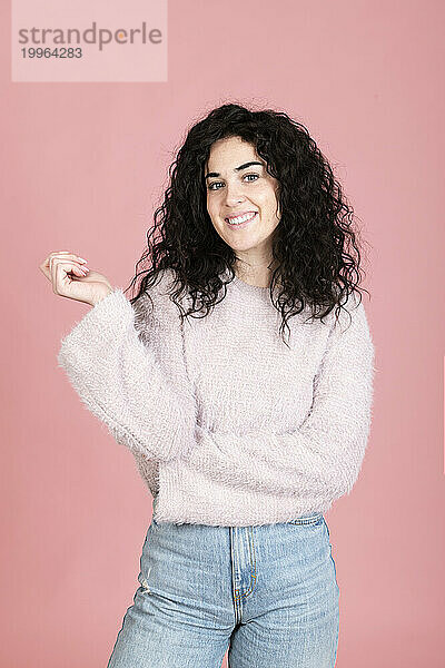 Happy young woman standing against pink background