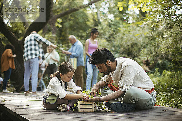 Junger Mann und Mädchen kontrollieren Kräuter im Gemeinschaftsgarten  sitzend auf der Promenade