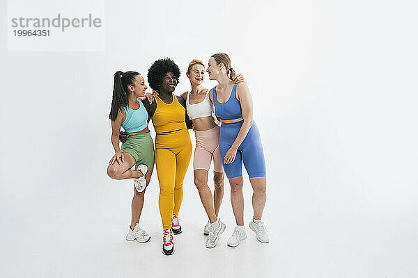 Happy multiracial female friends standing together against white background