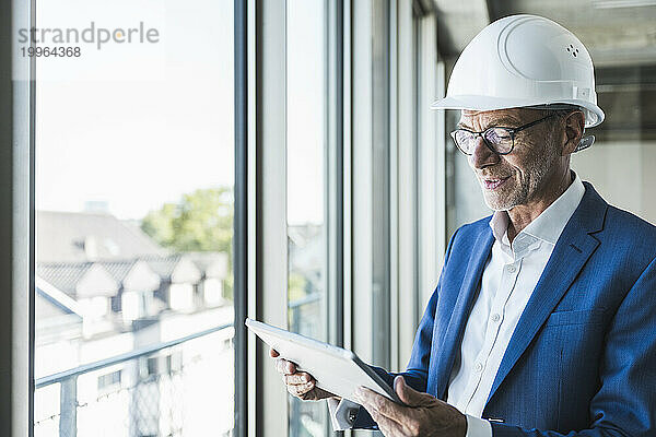 Lächelnder Ingenieur benutzt Tablet-PC am Fenster