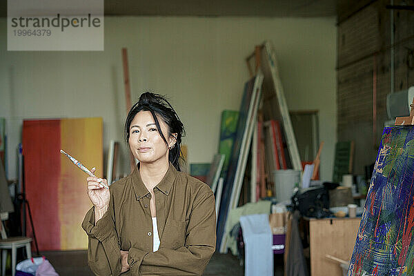 Selbstbewusster Maler hält Pinsel in der Hand und malt in der Werkstatt