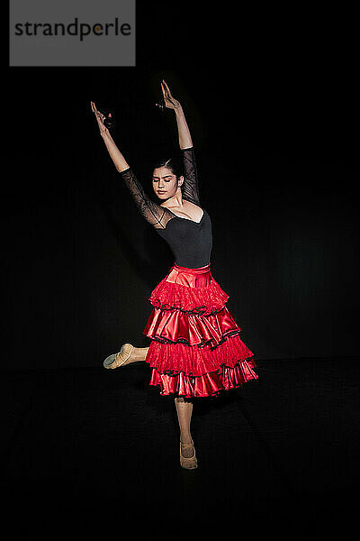 Schöne Frau beim Flamenco-Tanz in rotem Rock vor schwarzem Hintergrund