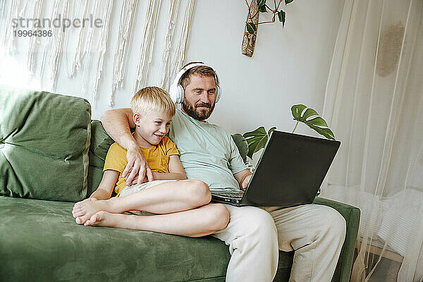 Father and son looking at a laptop while sitting on the couch at home
