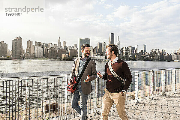 Fröhliche junge Kollegen unterhalten sich am Fluss vor der Skyline von New York City