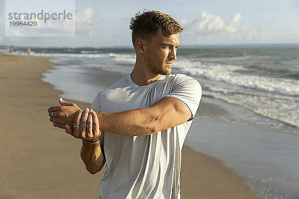 Junger Mann streckt am Strand den Arm aus