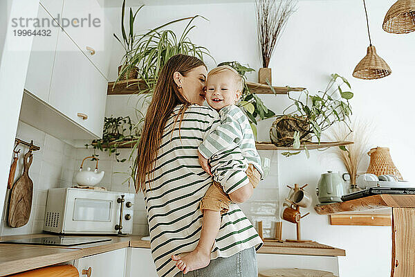 Mother carrying son in kitchen at home