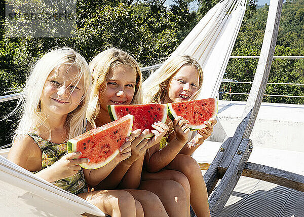 Lächelnde Schwestern sitzen auf einer Hängematte mit Wassermelonenscheiben