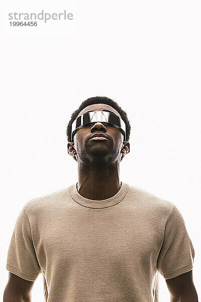 Cooler junger Mann mit Cyberbrille vor weißem Hintergrund  der nach oben schaut