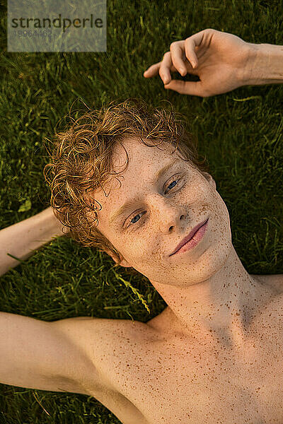 Lächelnde nicht-binäre Person mit Sommersprossen  die im Gras liegt