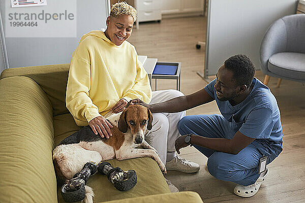 Glückliche Frau mit Tierarzt  der Hund auf dem Sofa in der Klinik streichelt