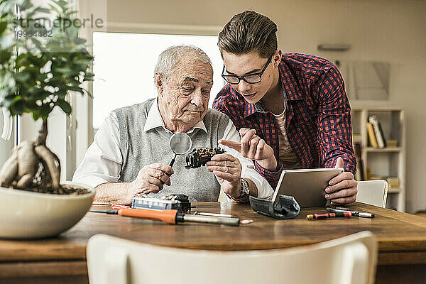 Junger Mann hilft Großvater bei der Reparatur eines Miniaturzuges zu Hause