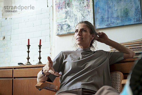 Selbstbewusste Frau sitzt auf einem Stuhl vor Gemälden in der Werkstatt