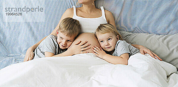 Children leaning on pregnant mother's stomach at home