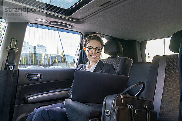 Lächelnde Geschäftsfrau benutzt Laptop im Auto