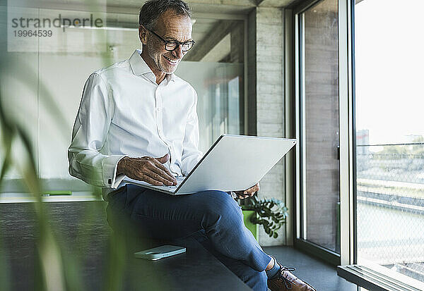 Glücklicher Geschäftsmann mit Laptop und Smartphone auf dem Schreibtisch