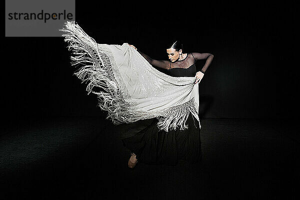 Young flamenco dancer performing with shawl against black background